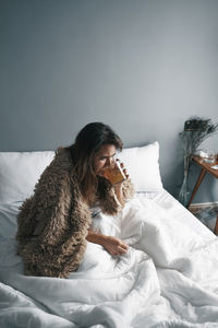 High angle view of woman drinking lemon tea sitting on bed