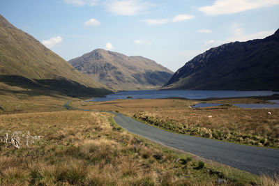 Scenic view of road by mountains against sky