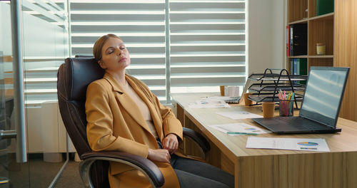 Tired business woman lying on chair and closing her eyes after hard working day. 