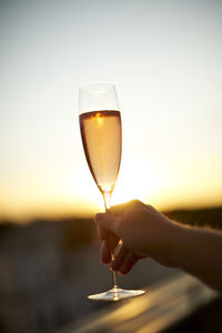 Close-up of hand holding wineglass against sunset