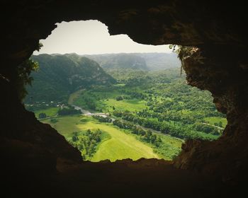 Scenic view of green landscape and mountains seen through cave