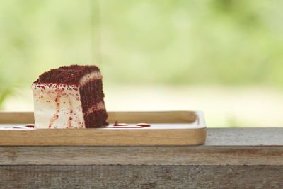 Close-up of red velvet cheesecake slice in wooden plate on table outdoors