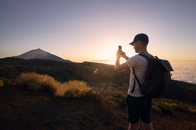 Man photograps by mobile phone against landscape at sunset. volcano pico de teide, tenerife, spain.