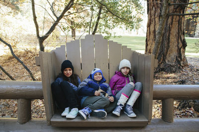 Portrait of siblings wearing warm clothing sitting in wooden seat at yosemite national park