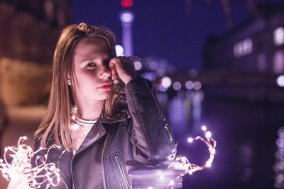 Young woman with illuminated string lights in city at night