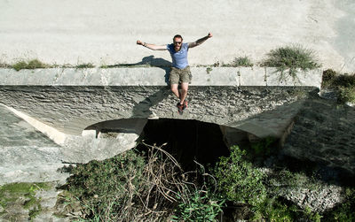 Young man with arms raised sitting on retaining wall