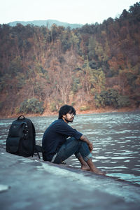 Young man sitting on rock by lake