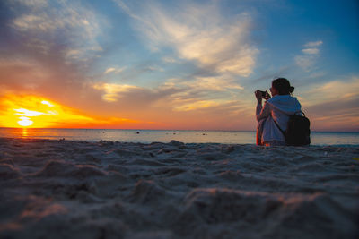 Man photographing at beach against sky during sunset