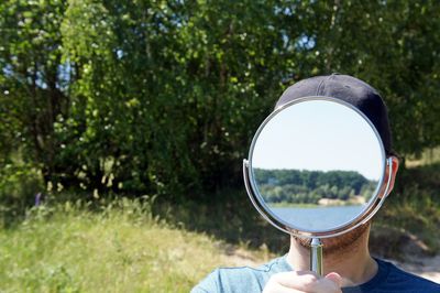 Headshot of man standing with mirror covering face