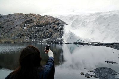 Rear view of woman photographing in lake against sky
