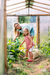 A young mother and her little daughter together water the plants in the greenhouse. childhood