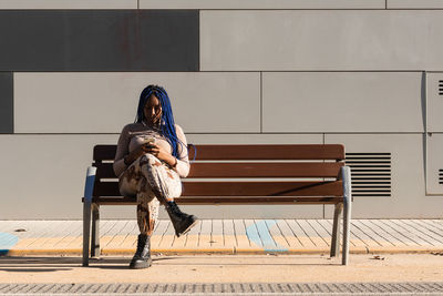 Full length of woman sitting on bench against wall