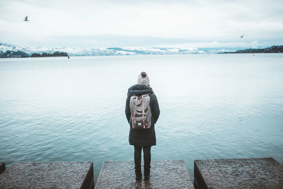 Rear view of man standing by sea against sky