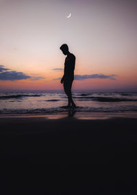 Silhouette man standing at beach against sky during sunset