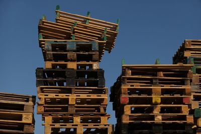 Low angle view of stacked wooden pallets against clear blue sky