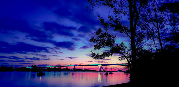 Silhouette trees by lake against sky at sunset