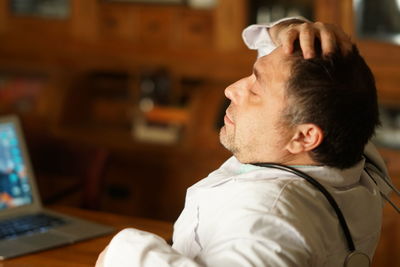 Side view of tensed mature doctor sitting in hospital