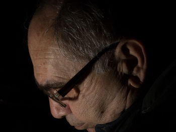Close-up of mature man wearing eyeglasses against black background