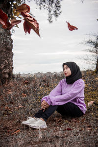 Woman sitting on field against sky