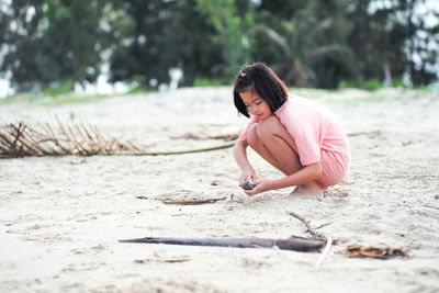 Portrait asian girl plays the shell at the beach with blurred tree background