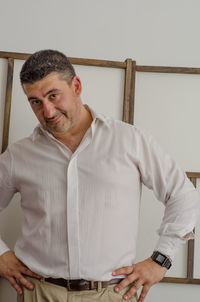 Portrait of smiling man standing with hands on hip against wall at home