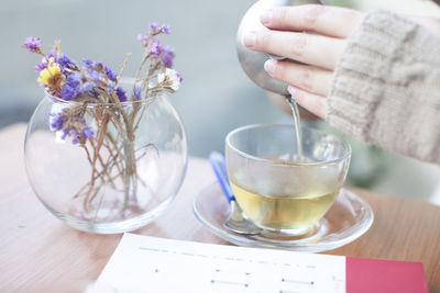 Cropped image of woman pouring tea in cup from kettle at cafe
