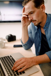 Worried businessman using laptop while sitting at creative office