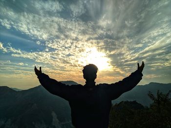 Rear view of silhouette man standing on mountain against sky