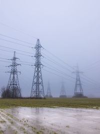 Electricity pylons on field against sky