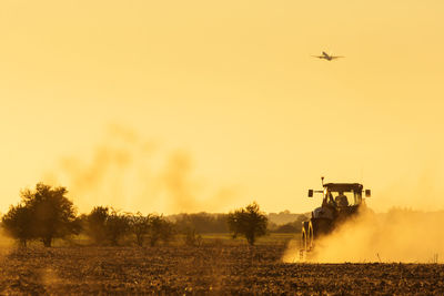 Airplane flying over field against sky during sunset