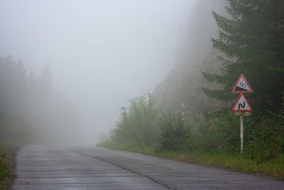 Red triangle road sign on the forest road in the fog