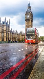 Double-decker bus on city street by big ben against sky