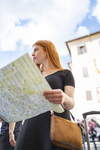 Young lady is searching for a direction using a paper map of the city