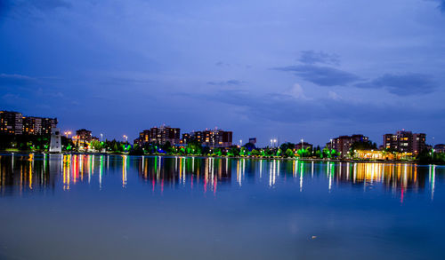 Illuminated buildings by lake against sky at dusk