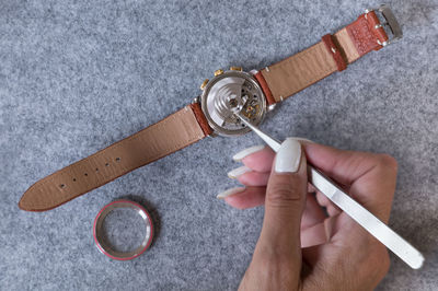 Cropped hand of woman repairing wristwatch on table