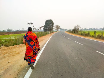 Rear view of woman walking on road against sky