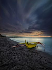 Boat moored on beach against sky during sunset