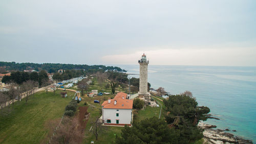 Lighthouse amidst trees and buildings against sky