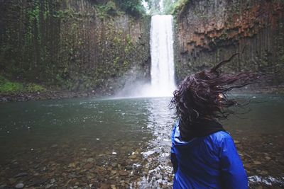 Rear view of man standing by waterfall in forest