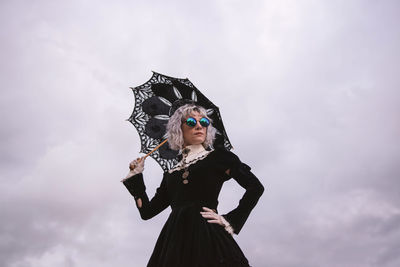 Low angle view of woman holding umbrella while standing against cloudy sky
