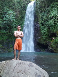 Full length of shirtless man standing on rock in forest