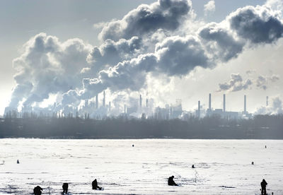 People on snow covered field with smoke emitting from chimneys against sky