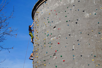 Low angle view of man and woman climbing on wall against sky