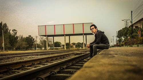 Man sitting on railroad track against sky