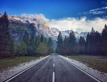 Road by trees on mountain against sky