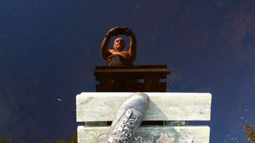 Low section of man taking photo of own reflection in water