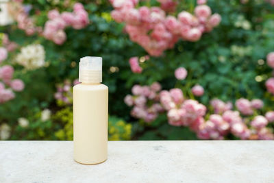 Yellow cosmetic bottle on concrete near pink flowers 