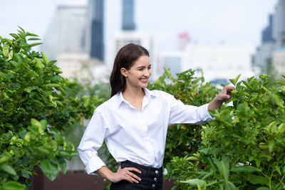 Smiling young woman standing against plants