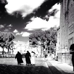 People walking in city against cloudy sky