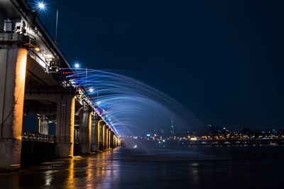 Light trails on bridge in city against sky at night